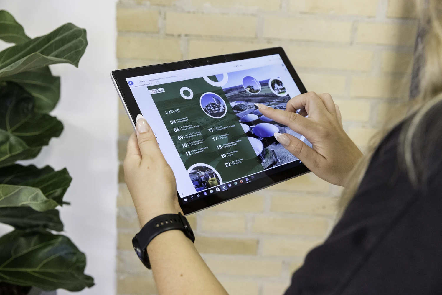 A woman is standing with a tablet an swiping through an interactive brochure.